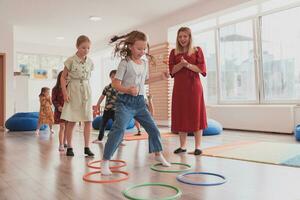 pequeno berçário escola crianças com fêmea professor em chão dentro de casa dentro sala de aula, fazendo exercício. pulando sobre hula aro círculos rastrear em a chão. foto