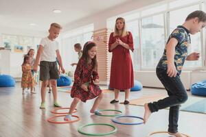 pequeno berçário escola crianças com fêmea professor em chão dentro de casa dentro sala de aula, fazendo exercício. pulando sobre hula aro círculos rastrear em a chão. foto