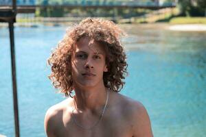 retrato do uma jovem adolescente Garoto com encaracolado molhado cabelo perto a rio tendo Diversão com amigos às uma verão Festa. foto