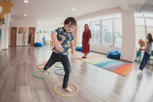 pequeno berçário escola crianças com fêmea professor em chão dentro de casa dentro sala de aula, fazendo exercício. pulando sobre hula aro círculos rastrear em a chão. foto