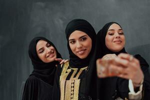 grupo do jovem lindo muçulmano mulheres dentro elegante vestir com hijab usando Smartphone enquanto levando selfie cenário dentro frente do Preto fundo foto