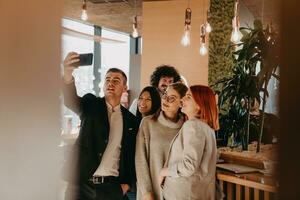grupo de colegas alegres tomando selfie e gesticulando em pé no escritório moderno. foto