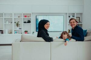 feliz muçulmano família com filha mulher dentro tradicional elegante vestir tendo Diversão e Boa Tempo juntos enquanto sentado em sofá foto