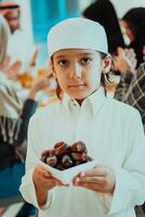 eid Mubarak muçulmano família tendo iftar jantar pequeno Garoto segurando uma prato cheio do doce datas para pausa celebração. comendo tradicional Comida durante Ramadã festa mês às lar. a islâmico halal comendo foto