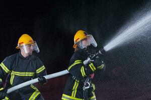 bombeiros usando uma água mangueira para eliminar uma fogo perigo. equipe do fêmea e masculino bombeiros dentro perigoso resgate missão. foto