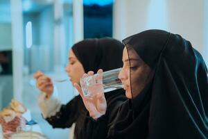 eid Mubarak muçulmano família tendo iftar jantar bebendo água para pausa celebração. comendo tradicional Comida durante Ramadã festa mês às lar. a islâmico halal comendo e bebendo às moderno ocidental isla foto