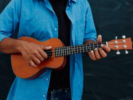 indiano jovem homem dentro uma azul camisa e óculos jogando a guitarra dentro frente do a escola quadro-negro foto