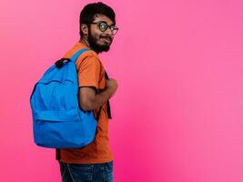 indiano aluna com azul mochila, óculos e caderno posando em Rosa fundo. a conceito do Educação e escolaridade. Tempo para ir costas para escola foto