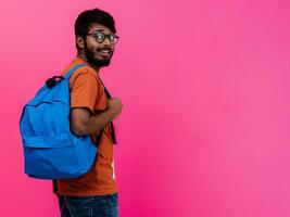 indiano aluna com azul mochila, óculos e caderno posando em Rosa fundo. a conceito do Educação e escolaridade. Tempo para ir costas para escola foto