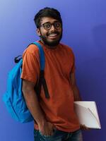 indiano aluna com azul mochila, óculos e caderno posando em roxa fundo. a conceito do Educação e escolaridade. Tempo para ir costas para escola foto