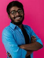 indiano sorridente jovem homem com azul camisa e óculos posando em Rosa fundo foto