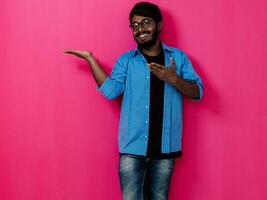 indiano sorridente jovem aluna dentro azul camisa e óculos posando em Rosa fundo foto