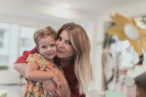 uma fofa pequeno menina Beijos e abraços dela mãe dentro pré escola foto