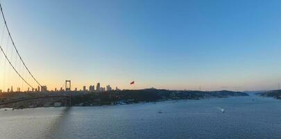 Istambul bósforo ponte e cidade Horizonte dentro fundo com turco bandeira às lindo pôr do sol, aéreo deslizar órbita e rastreamento tiro foto