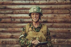 mulher soldado usando tábua computador contra velho de madeira parede dentro acampamento foto