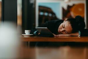 uma mulher com sono senta-se em um café durante uma pausa e usa um conceito tablet.business. foto