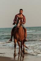 um homem moderno em roupas de verão gosta de andar a cavalo em uma bela praia ao pôr do sol. foco seletivo foto