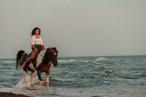 mulher com roupas de verão gosta de andar a cavalo em uma bela praia ao pôr do sol. foco seletivo foto