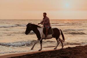 um homem moderno em roupas de verão gosta de andar a cavalo em uma bela praia ao pôr do sol. foco seletivo foto