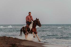 um homem moderno em roupas de verão gosta de andar a cavalo em uma bela praia ao pôr do sol. foco seletivo foto