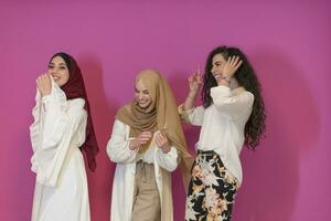 três muçulmano mulheres dentro hijab dentro uma moderno roupas pose contra uma Rosa fundo foto