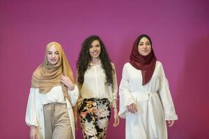 três muçulmano mulheres dentro hijab dentro uma moderno roupas pose contra uma Rosa fundo foto