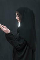 retrato do lindo muçulmano mulher dentro elegante vestir com hijab fazer tradicional oração para Deus mantém mãos dentro Rezar gesto isolado em Preto fundo foto