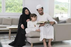 tradicional muçulmano família pais com crianças lendo Alcorão e Rezar juntos em a sofá antes iftar jantar durante uma Ramadã festa às casa foto