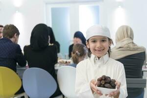 eid Mubarak muçulmano família tendo iftar jantar pequeno Garoto segurando uma prato cheio do doce datas para pausa celebração. comendo tradicional Comida durante Ramadã festa mês às lar. a islâmico halal comendo foto