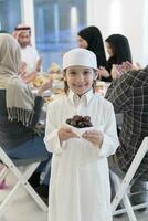 eid Mubarak muçulmano família tendo iftar jantar pequeno Garoto segurando uma prato cheio do doce datas para pausa celebração. comendo tradicional Comida durante Ramadã festa mês às lar. a islâmico halal comendo foto