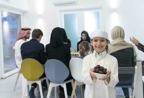 eid Mubarak muçulmano família tendo iftar jantar pequeno Garoto segurando uma prato cheio do doce datas para pausa celebração. comendo tradicional Comida durante Ramadã festa mês às lar. a islâmico halal comendo foto