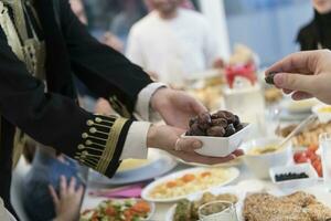 moderno multiétnico muçulmano família partilha uma tigela do datas enquanto desfrutando iftar jantar juntos durante uma Ramadã festa às casa foto