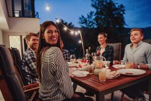 uma grupo do jovem diverso pessoas tendo jantar em a terraço do uma moderno casa dentro a tarde. Diversão para amigos e família. celebração do feriados, casamentos com churrasco. foto