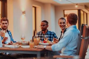 uma grupo do jovem diverso pessoas tendo jantar em a terraço do uma moderno casa dentro a tarde. Diversão para amigos e família. celebração do feriados, casamentos com churrasco. foto