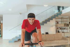 uma homem equitação uma triatlo bicicleta em uma máquina simulação dentro uma moderno vivo sala. Treinamento durante pandemia condições. foto