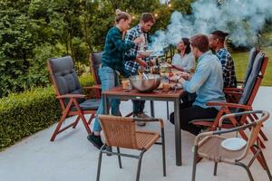 uma grupo do jovem diverso pessoas tendo jantar em a terraço do uma moderno casa dentro a tarde. Diversão para amigos e família. celebração do feriados, casamentos com churrasco. foto