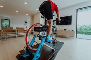 uma homem equitação uma triatlo bicicleta em uma máquina simulação dentro uma moderno vivo sala. Treinamento durante pandemia condições. foto