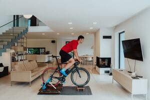 uma homem equitação uma triatlo bicicleta em uma máquina simulação dentro uma moderno vivo sala. Treinamento durante pandemia condições. foto