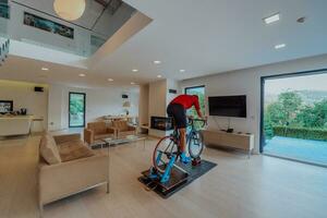 uma homem equitação uma triatlo bicicleta em uma máquina simulação dentro uma moderno vivo sala. Treinamento durante pandemia condições. foto