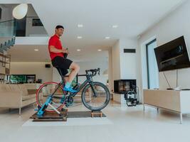 uma homem equitação uma triatlo bicicleta em uma máquina simulação dentro uma moderno vivo sala. Treinamento durante pandemia condições. foto