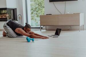 Treinamento às lar. desportivo homem fazendo Treinamento enquanto assistindo conectados tutorial em computador portátil, exercício dentro vivo sala, livre espaço foto