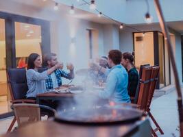 uma grupo do jovem diverso pessoas tendo jantar em a terraço do uma moderno casa dentro a tarde. Diversão para amigos e família. celebração do feriados, casamentos com churrasco. foto