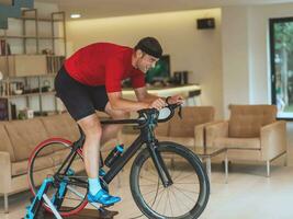 uma homem equitação uma triatlo bicicleta em uma máquina simulação dentro uma moderno vivo sala. Treinamento durante pandemia condições. foto