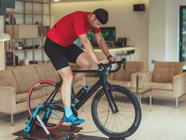 uma homem equitação uma triatlo bicicleta em uma máquina simulação dentro uma moderno vivo sala. Treinamento durante pandemia condições. foto