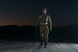 exército soldado dentro combate uniformes com a assalto rifle, prato transportadora e combate capacete indo em uma perigoso missão em uma chuvoso noite. foto