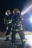 bombeiros usando uma água mangueira para eliminar uma fogo perigo. equipe do fêmea e masculino bombeiros dentro perigoso resgate missão. foto