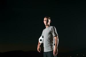 retrato do uma jovem bonito futebol jogador homem em uma rua jogando com uma futebol bola. foto