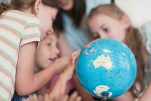 fêmea professor com crianças dentro geografia classe olhando às globo. lado Visão do grupo do diverso feliz escola crianças com globo dentro Sala de aula às escola. foto