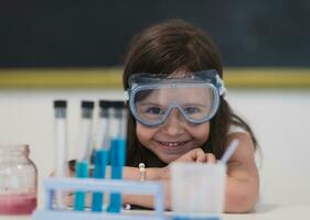 elementar escola Ciência Sala de aula pequeno menina mistura produtos químicos dentro copos. crianças aprender com interesse foto