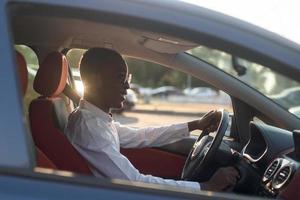 feliz afro-americano dirigindo um carro com um telefone, no verão foto